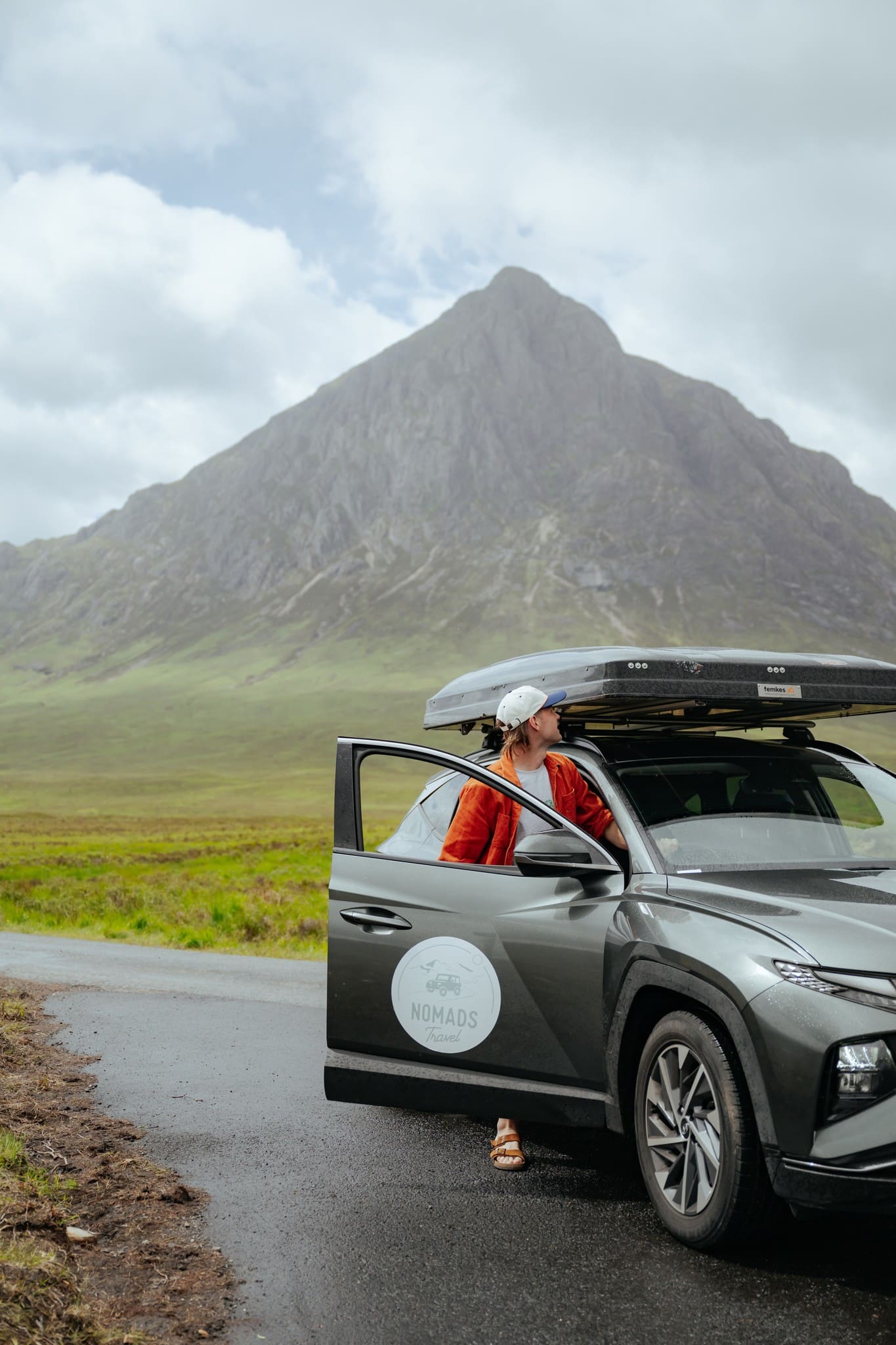 person in car with rooftop tent looking at mountain in Scotland