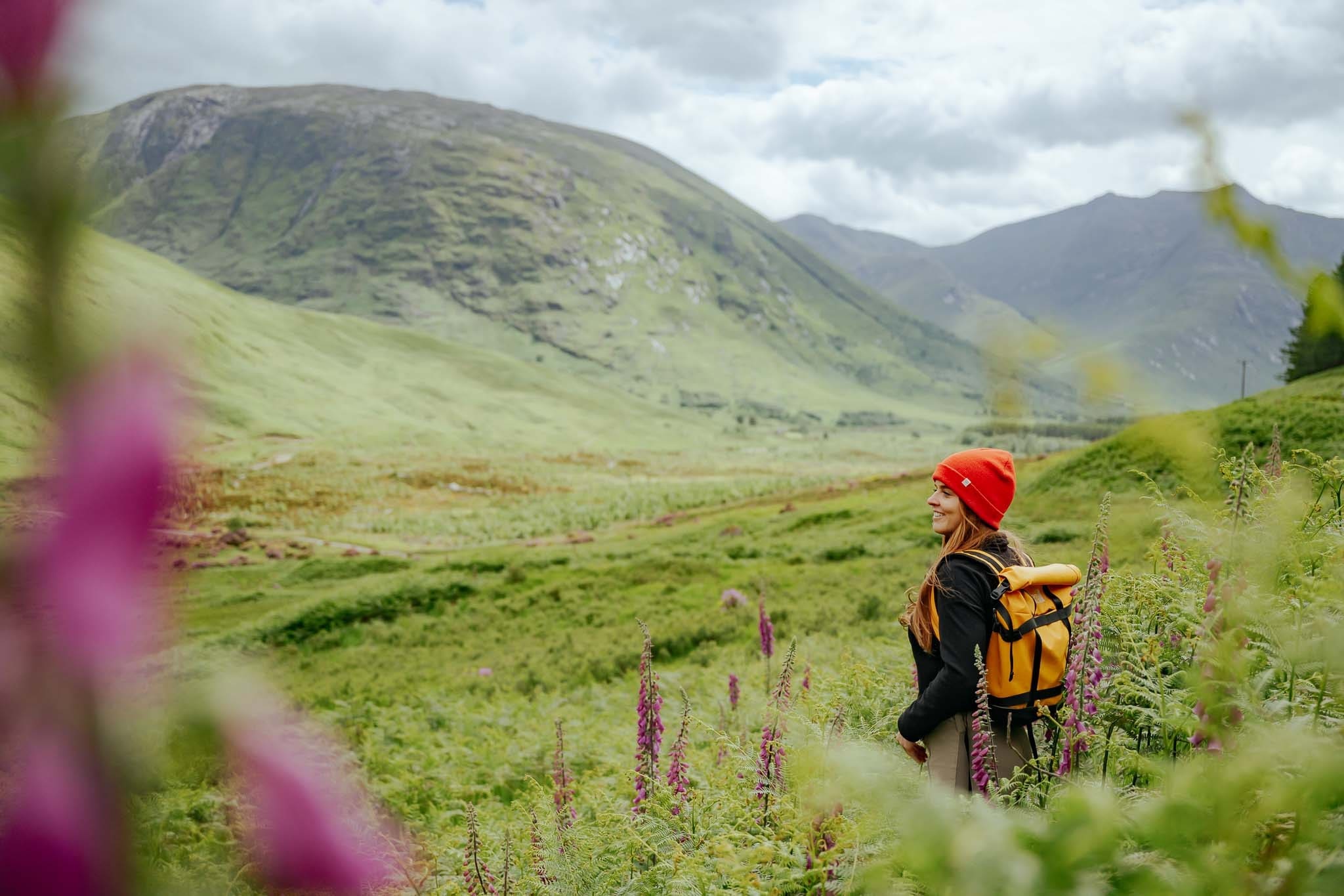 woman hiking in Scottish Highlands with red beanie and yellow backpack