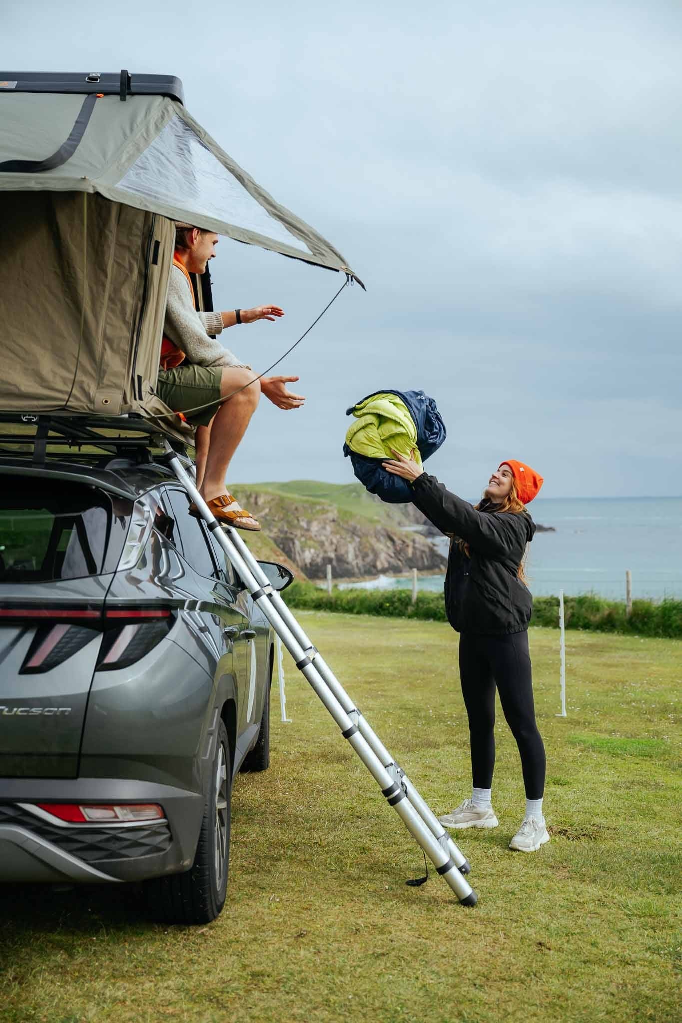 couple setting up rooftop tent on car by the coast in Scotland
